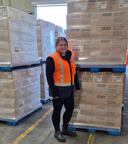 Female warehouse worker standing by stacked pallets of boxes
