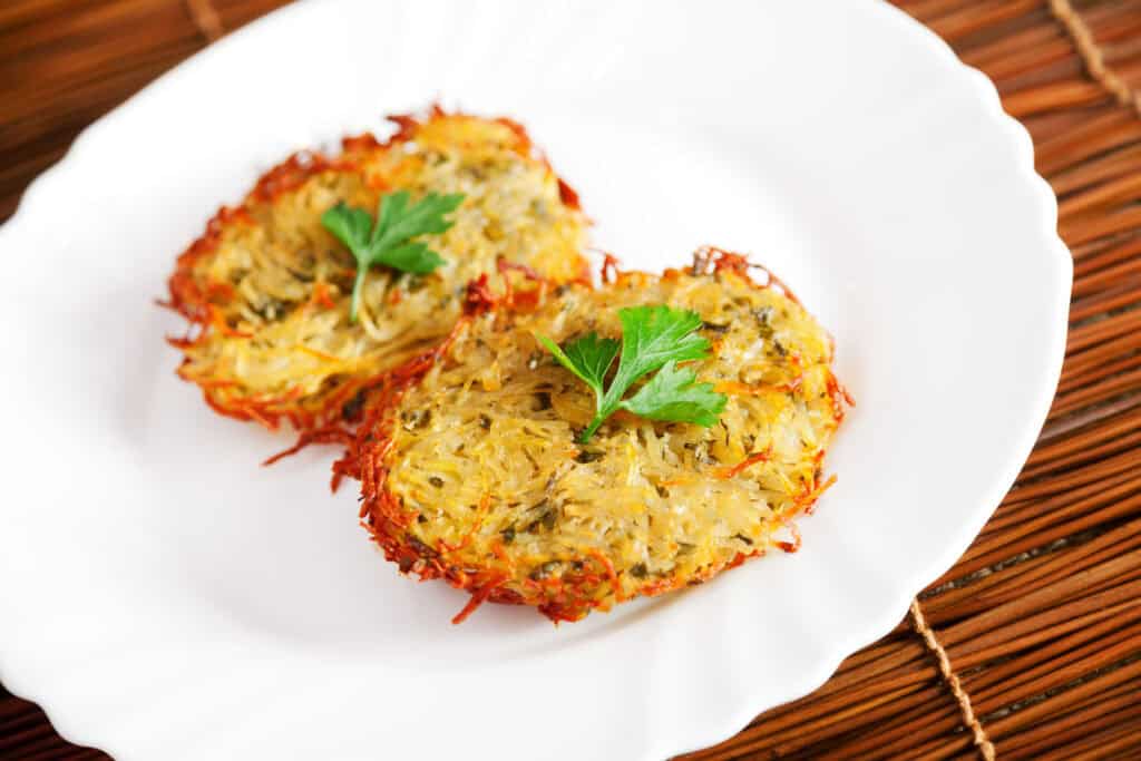 Two crispy herb potato latkes garnished with parsley on white plate