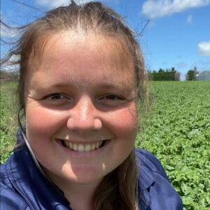 Smiling woman in blue jacket in green field under blue sky