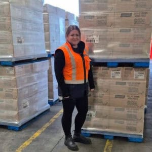 Warehouse worker in orange safety vest standing by pallets
