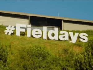 Large white hashtag Fieldays sign on grassy hillside outside building