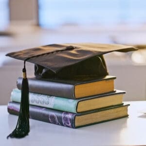 Stack of books with black graduation cap on top on table