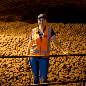 Smiling worker in orange vest standing with harvested sweet potatoes