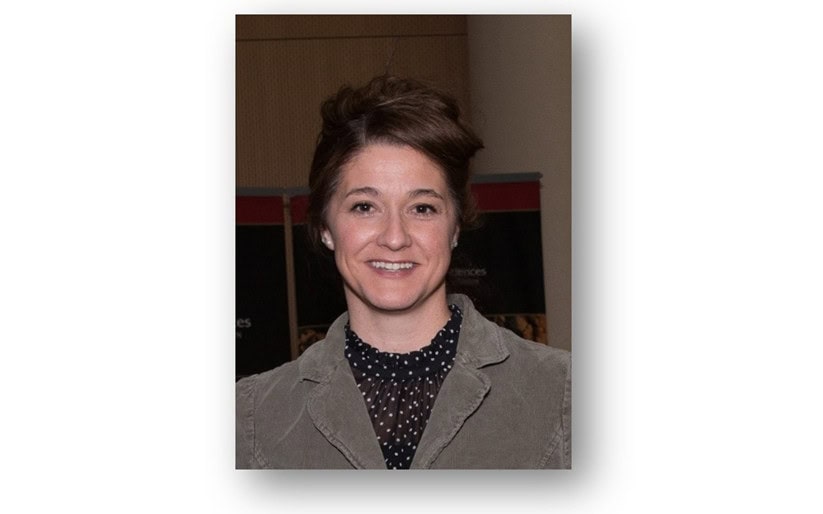 Smiling woman with brown hair wearing gray jacket and polka dot blouse