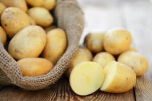 Fresh yellow potatoes spilling out of burlap sack on wooden surface