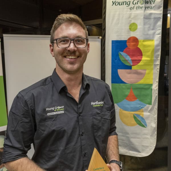Young grower holding award trophy at horticulture event banner