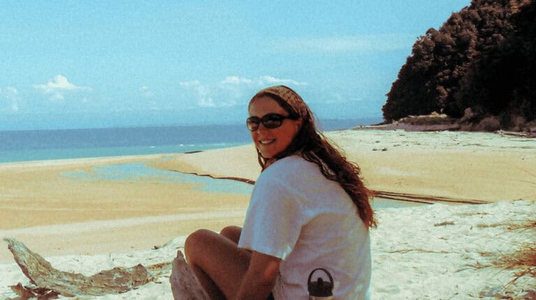 Woman wearing sunglasses sitting on sandy beach with ocean view