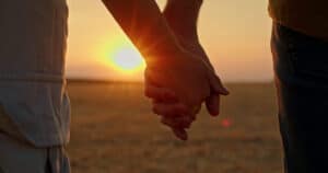 Couple holding hands during sunset in outdoor field.
