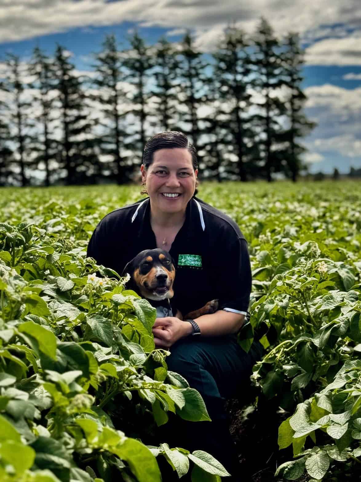Smiling woman holding dog in green field with trees background