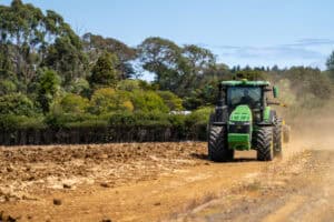 Green tractor plowing dry field with trees and clear sky background