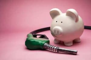 White piggy bank with green fuel pump nozzle on pink background