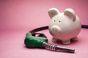 Piggy bank next to green fuel pump nozzle on pink background