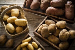 Assorted fresh potatoes in baskets and wooden trays on table